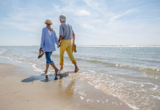 Ouder echtpaar loopt hand in hand op het strand bij Breeduyn Village 3 in België, zonnig weer.