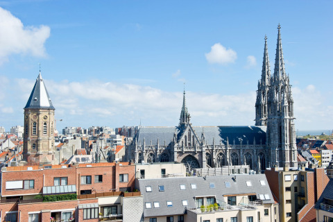 Uitzicht vanuit Breeduyn Village 3 in België, met een gotische kerk en moderne appartementen onder blauwe lucht.