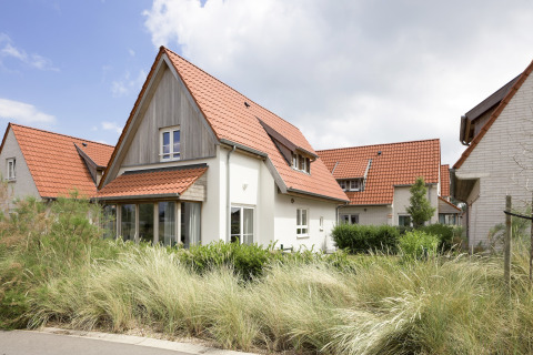 Moderne lodge in Breeduyn Village 3, België, met rood pannendak, grote ramen en groene tuin aan de voorkant.