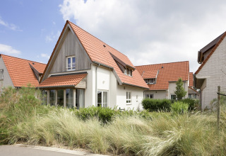Moderne lodge in Breeduyn Village 3, België, met rood pannendak, grote ramen en groene tuin aan de voorkant.