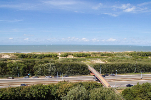 Uitzicht vanaf Breeduyn Village 3 in België met de zee, strand, groen, weg en voetgangersbrug.