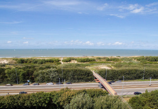 Uitzicht vanaf Breeduyn Village 3 in België met de zee, strand, groen, weg en voetgangersbrug.