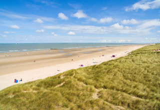 Strandzicht vanaf de lodge Breeduyn Village 3 in België met zandduinen, zee en blauwe lucht.