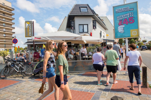 Mensen lopen langs een terras bij Breeduyn Village 3 op een zonnige dag in België.