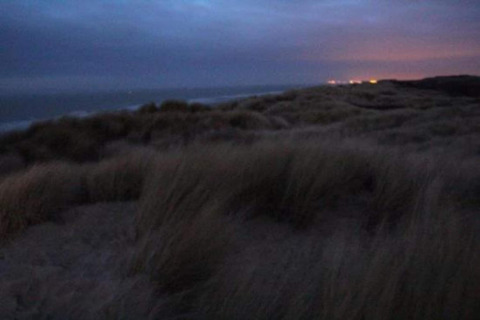 Schemerzicht op grasduinen en zee bij Breeduyn Village 3 lodge in België, lichtjes zichtbaar in verte.