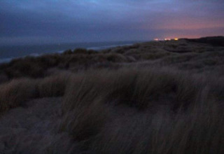Schemerzicht op grasduinen en zee bij Breeduyn Village 3 lodge in België, lichtjes zichtbaar in verte.