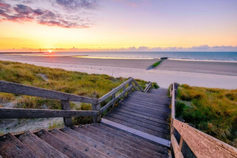 Houten trap loopt naar een rustige strand bij zonsondergang bij Breeduyn Village 3 lodge in België.