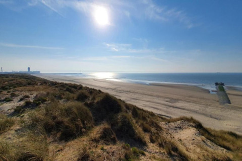 Zonnig strandzicht vanaf de duinen bij Breeduyn Village 3 in België, met uitzicht op zee en kustlijn.