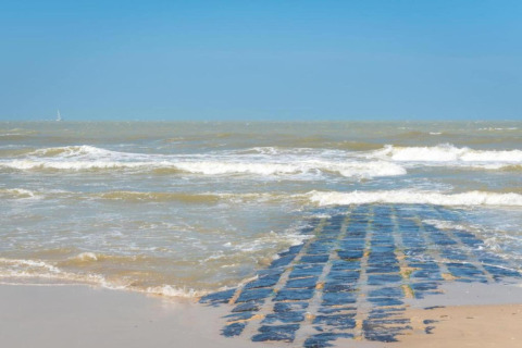 Een stenen pad loopt de zee in bij Breeduyn Village 3 in België, met golven en een heldere lucht.
