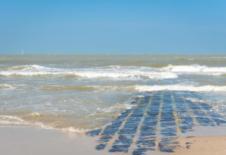 Een stenen pad loopt de zee in bij Breeduyn Village 3 in België, met golven en een heldere lucht.