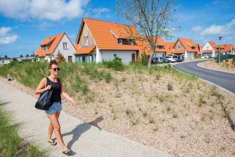Vrouw wandelt op het pad naast vakantiehuizen met oranje daken in Breeduyn Village 3, België op zonnige dag.