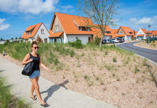 Vrouw wandelt op het pad naast vakantiehuizen met oranje daken in Breeduyn Village 3, België op zonnige dag.