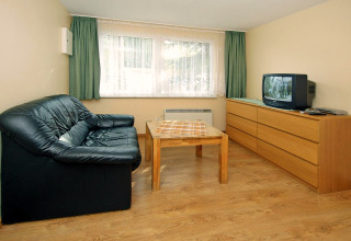 Woonkamer in Bungalow «35 qm 2 Pers» in Duitsland met zwarte zetel, tafel en tv op dressoir.