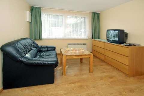 Woonkamer in Bungalow «35 qm 2 Pers» in Duitsland met zwarte zetel, tafel en tv op dressoir.