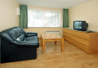 Woonkamer in Bungalow «35 qm 2 Pers» in Duitsland met zwarte zetel, tafel en tv op dressoir.