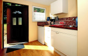 Cocina luminosa con suelo de madera, puerta abierta, electrodomésticos y salpicadero rojo mosaico.