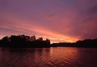Schitterende zonsondergang boven een rustig meer met bomen, gezien vanuit een glampingaccommodatie.