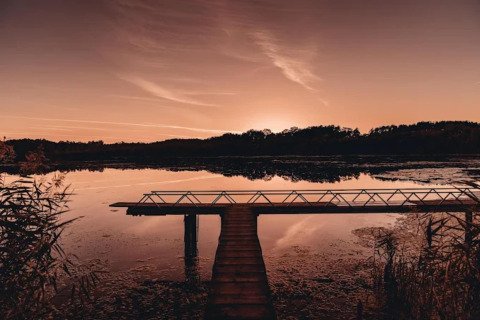 Zonsondergang boven een meer met houten pier bij een glampinglocatie, omgeven door rustige natuur.