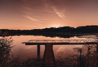 Zonsondergang boven een meer met houten pier bij een glampinglocatie, omgeven door rustige natuur.