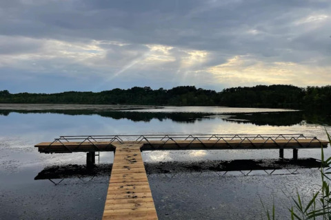 Afbeelding van een houten steiger aan een rustig meer met bewolkte lucht, genomen bij een glamping-verblijf.