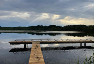 Foto di un molo in legno su un lago calmo con cielo nuvoloso, scattata presso una sistemazione glamping.