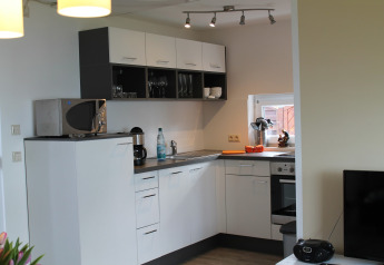 Modern kitchen with white cabinets, microwave, coffee maker, and window in a lodge in Germany.