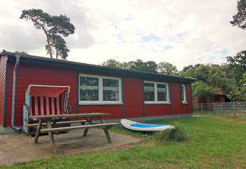 Rood vakantiehuis bij lodge 'Am Strand' in Duitsland, met bank, strandstoel en surfplank buiten.