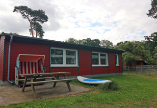 Rood vakantiehuis bij lodge 'Am Strand' in Duitsland, met bank, strandstoel en surfplank buiten.
