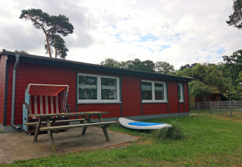 Red holiday cottage at 'Am Strand' lodge in Germany, with bench, beach chair, and surfboard outside.