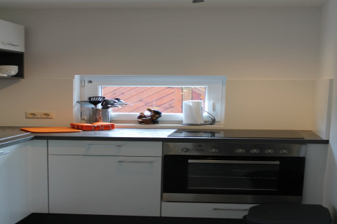 Moderne keuken in lodge Am Strand in Duitsland, met oven, kookplaat en een klein raampje.