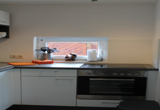 Moderne keuken in lodge Am Strand in Duitsland, met oven, kookplaat en een klein raampje.