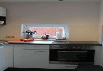 Modern kitchen at Am Strand lodge in Germany with oven, stovetop, and a small window view.