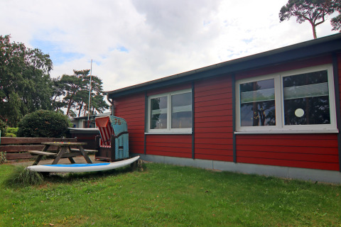 Buitenaanzicht van lodge 'Am Strand' in Duitsland met rode gevel, groen gras en picknicktafel.