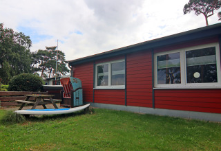 Buitenaanzicht van lodge 'Am Strand' in Duitsland met rode gevel, groen gras en picknicktafel.