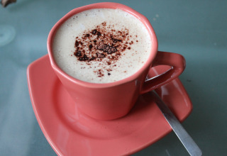 Kop koffie met melkschuim en cacaopoeder in een roze kop, geserveerd bij lodge «Am Strand» in Duitsland.