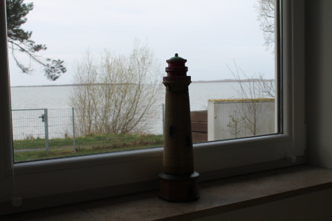 Lichttorenmodel op een vensterbank met uitzicht op meer en bomen bij Am Strand in Duitsland.