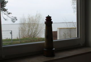 Lichttorenmodel op een vensterbank met uitzicht op meer en bomen bij Am Strand in Duitsland.