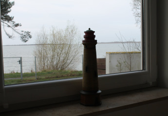 Model lighthouse on a windowsill overlooking a lake and trees at Am Strand lodge, Germany.
