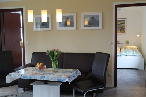 Eetruimte met bruine hoekbank, bloemen op tafel en zicht op slaapkamer in lodge 'Am Strand' in Duitsland.