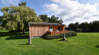 Bungalow in legno nel complesso Gänseblümchen 6, circondato da prato verde e grandi alberi.