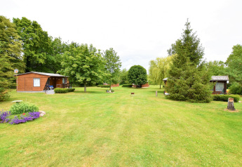Photo of a glamping accommodation with small wooden cabins, green grass, and many trees in the area.