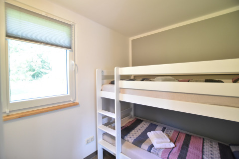 Chambre avec lits superposés et fenêtre au complexe de bungalows « Gänseblümchen 6 » en Allemagne.