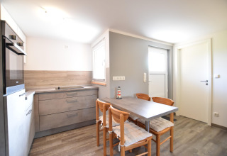 Lichte keuken met grijze kasten en eettafel voor vier in bungalowcomplex Gänseblümchen 6 in Duitsland.