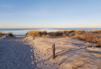 Beach view from a glamping accommodation showing sandy dunes, beach grass, and a calm sea at sunset.