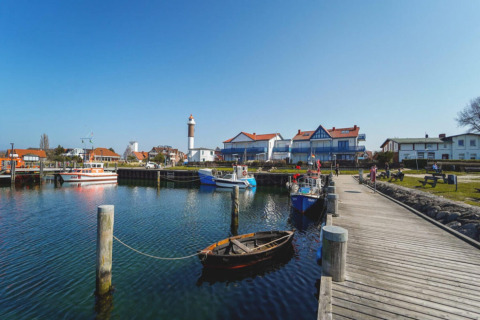 Port devant le complexe de bungalows Gänseblümchen 6 en Allemagne, bateaux, quai et phare en arrière-plan.