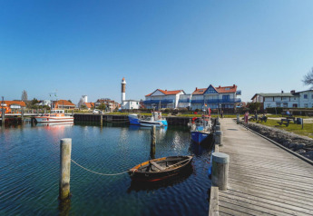 Harbor scene at Bungalow complex Gänseblümchen 6 in Germany with boats, pier, and a distant lighthouse.
