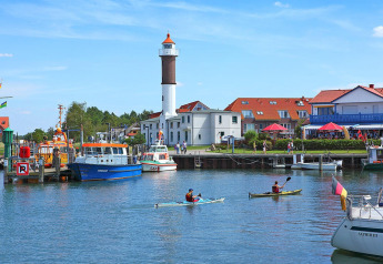 Harbor scene with boats, kayaks, a lighthouse, and red-roofed buildings at Gänseblümchen 6, Germany.