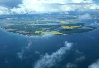 Aerial view of a scenic island with patchwork fields and coast, captured from a glamping accommodation.