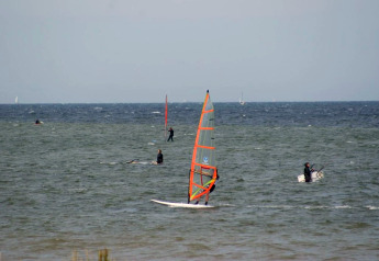People windsurfing and sailing on the sea near Bungalow complex «Gänseblümchen 6» in Germany on a windy day.
