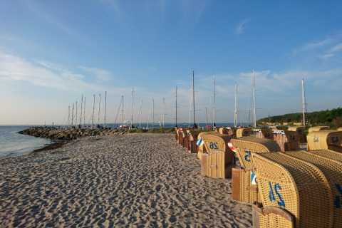 Spiaggia sabbiosa con sedie di vimini, barche a vela e cielo blu vicino al complesso «Gänseblümchen 6» in Germania.